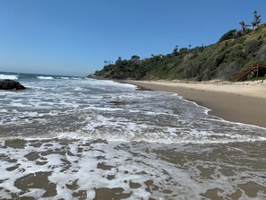 A beach with waves, a sandy shore, and a hillside with trees. - Cape Cod inspired Malibu Beach home (Malibu)
