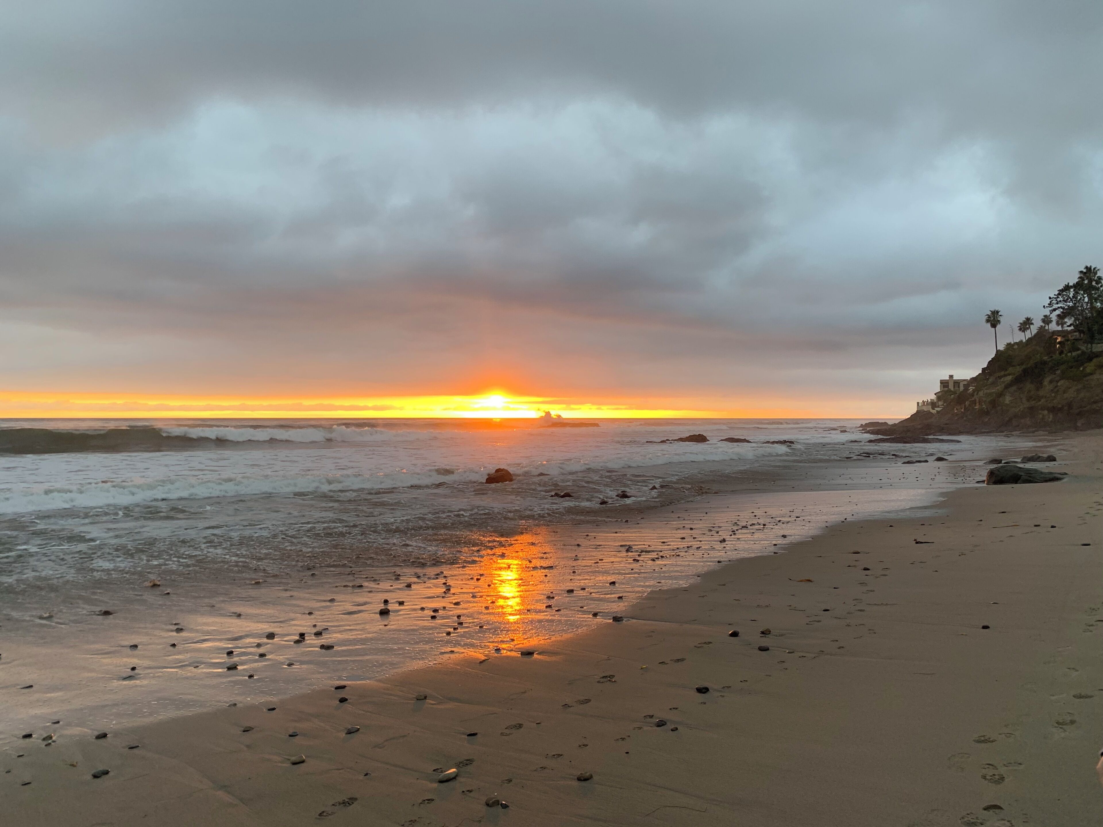 A beach with a sunset, ocean waves, and scattered rocks.