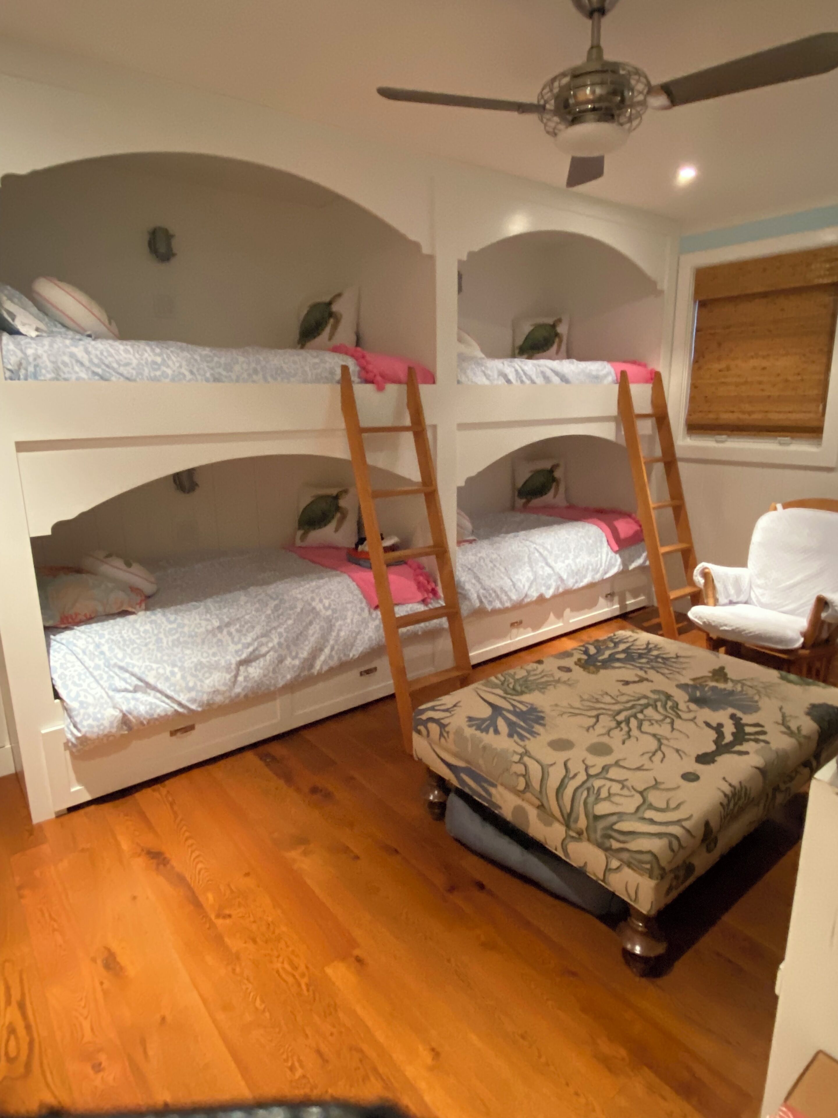 Une chambre avec un lit superposé, un ventilateur de plafond, une échelle en bois et une chaise.