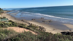 Vista costeira com uma praia arenosa, afloramentos rochosos e céu azul límpido.