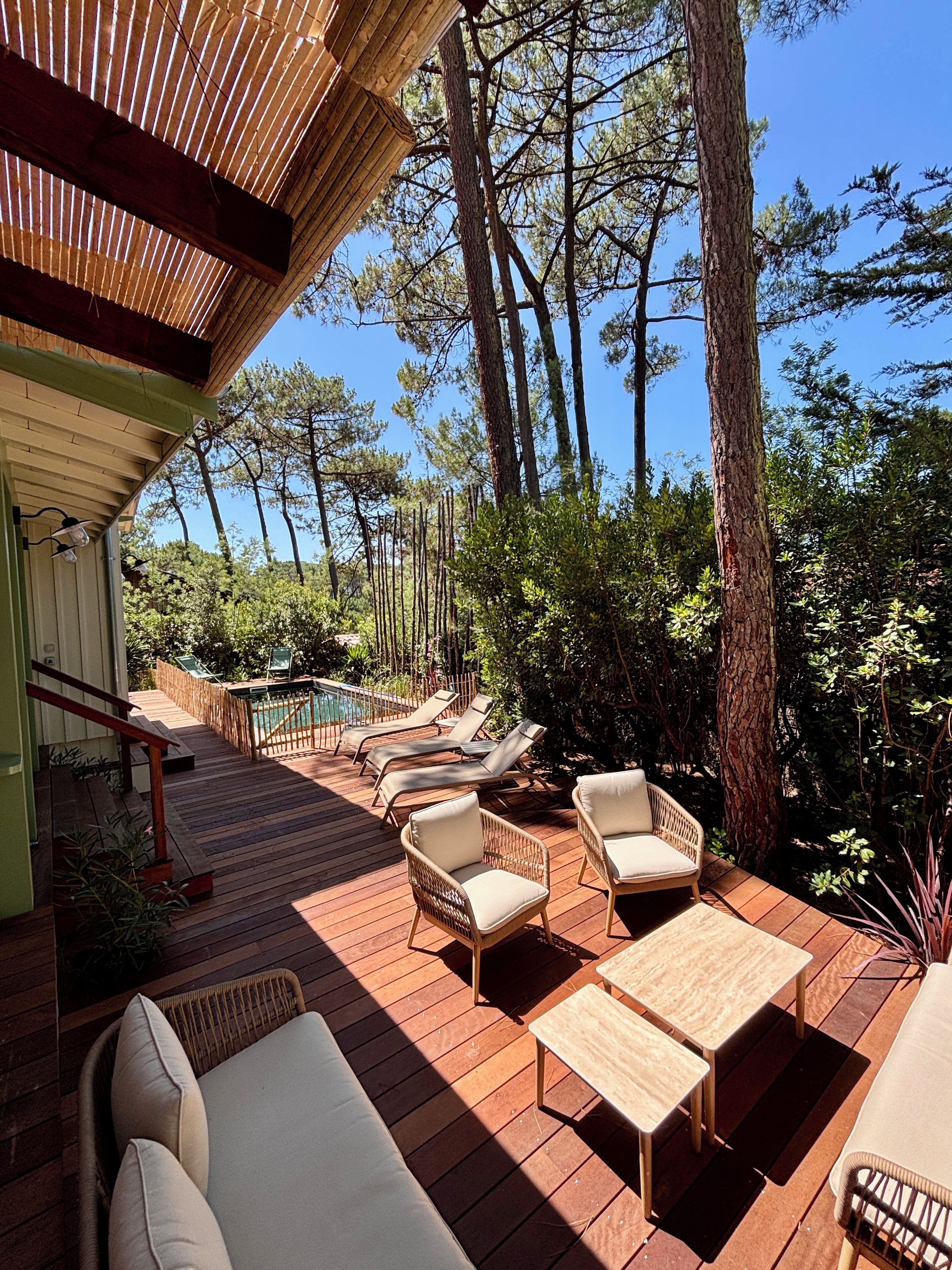 A wooden deck with outdoor furniture, a pool, and a view of tall trees.