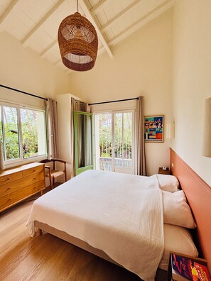 A bedroom with a bed, a wooden dresser, a chair, a window with curtains, a hanging light fixture, and a wall-mounted picture. - Le Canon – Beautiful, renovated villa in the Landes region with a pool – Sleeps 10 – Beach within walking distance (Lège-Cap-Ferret)