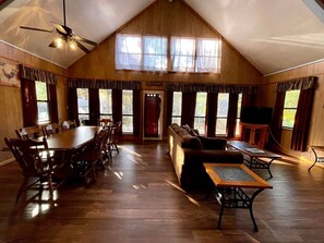 A spacious room with a high ceiling, wooden walls, a dining table with chairs, a sofa, and a television. - Spacious Luxury Cabin with Resort Amenities Near Zwolle, LA (Zwolle)