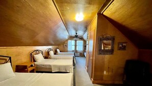 Ein Zimmer mit drei Betten, Holzwänden, einem Deckenventilator und einem Fenster mit Vorhängen.