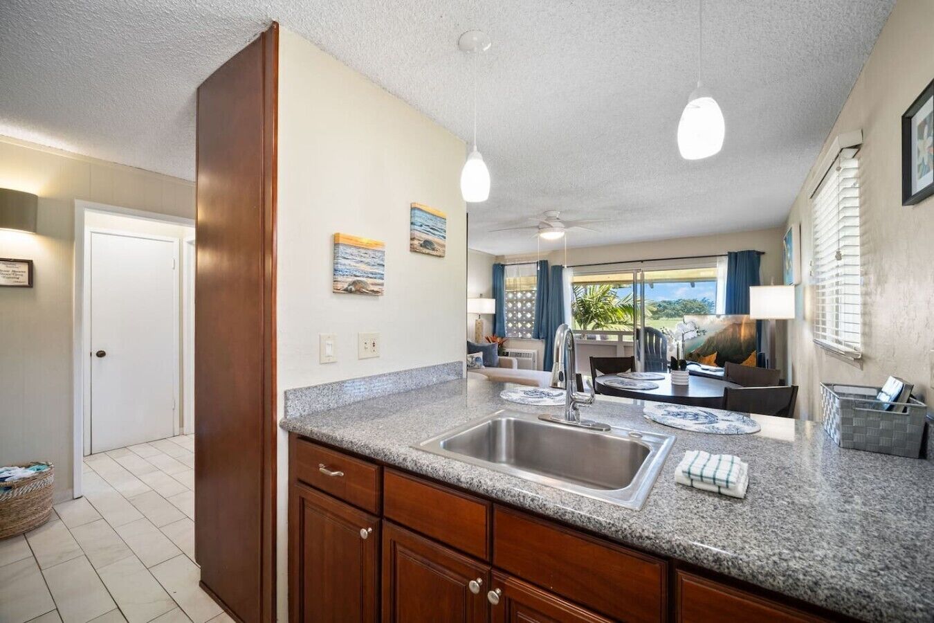 A kitchen with granite countertops, a stainless steel sink, wooden cabinets, pendant lighting, and a view of the outdoors through large windows.