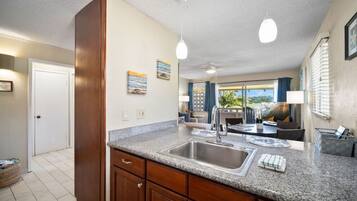 A kitchen with granite countertops, a stainless steel sink, wooden cabinets, pendant lighting, and a view of the outdoors through large windows.