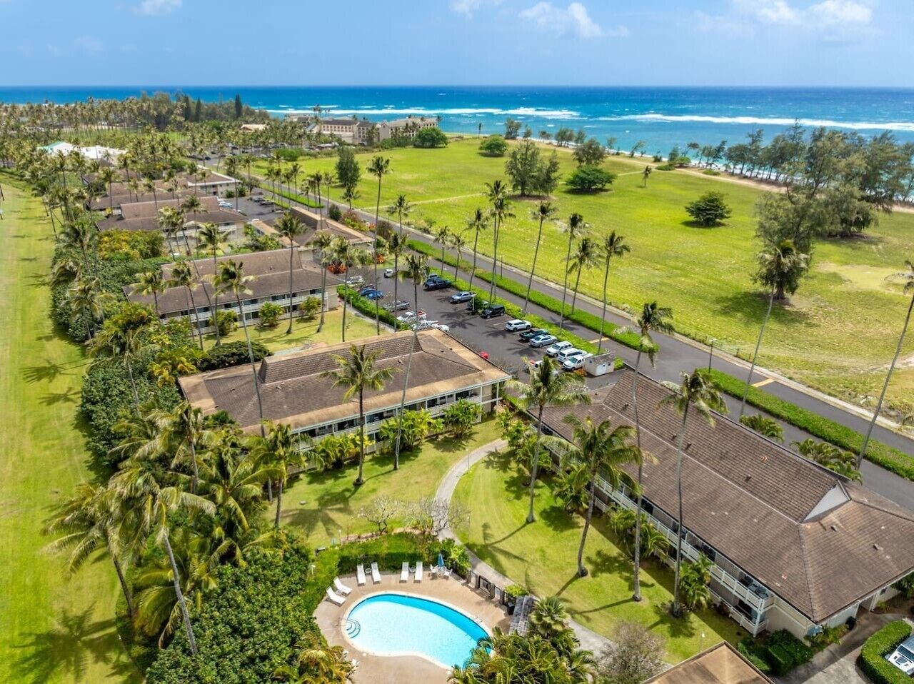 An aerial view of a resort with a swimming pool, multiple buildings, and a beachfront.