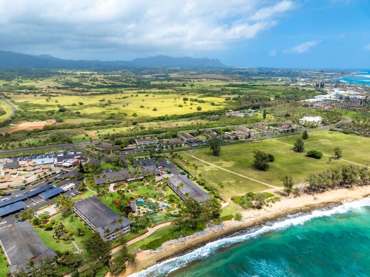 An aerial view of a coastal resort with multiple buildings, a beach, and a clear view of the ocean.