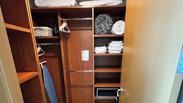 Een kleine kamer met een kledingkast, planken met opgevouwen handdoeken, een weegschaal en een hangrek.