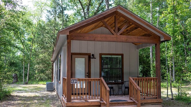 A wooden cabin with a porch, a door, and a window. - Picturesque Cabin Beautifully Designed in Livingston, Texas (Livingston)