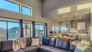A modern living room with a sectional sofa, a dining area, and a kitchen with large windows. - Sleeps 30! Spacious Luxury: Pools, Hot Tubs, Games (Canyon Lake)
