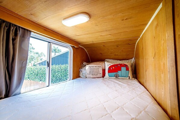 A small, enclosed sleeping area with a bed, a pillow with a camper van design, and a sign with instructions.