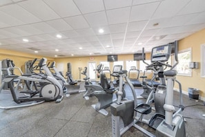 Una palestra con diverse macchine cardio, uno schermo televisivo e un soffitto piastrellato.
