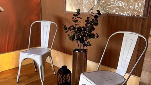 Dos sillas de metal blanco, un suelo de madera, una ventana con vistas y una planta en maceta.