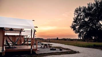A rustic outdoor seating area with hammocks and a covered picnic table, set against a sunset backdrop.