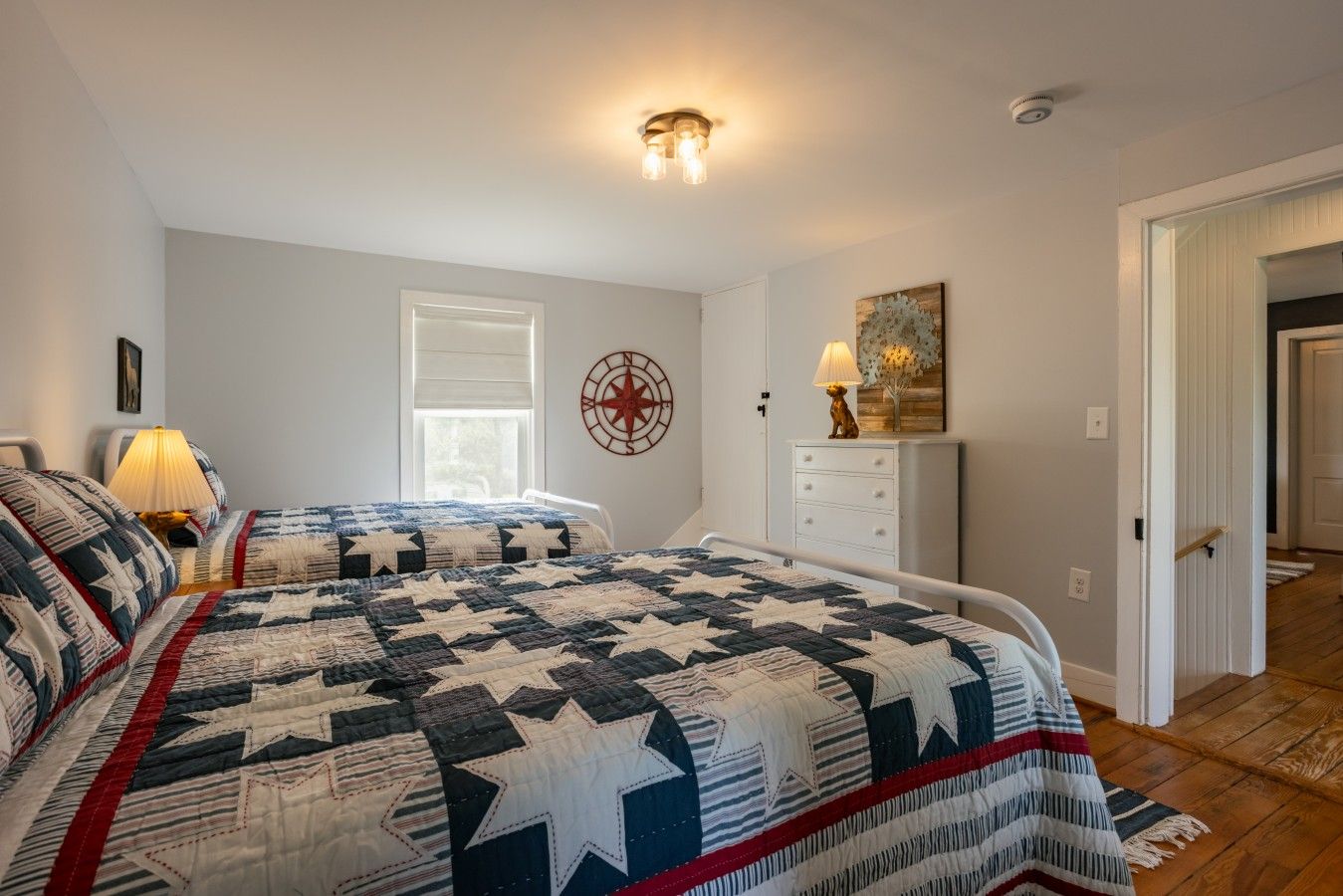 A bedroom with two beds, a compass wall decoration, a lamp, and a wooden floor.