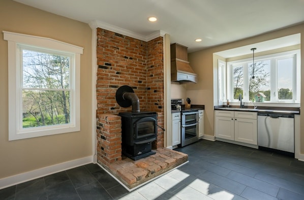 A modern kitchen with a brick fireplace, white cabinetry, and large windows.
