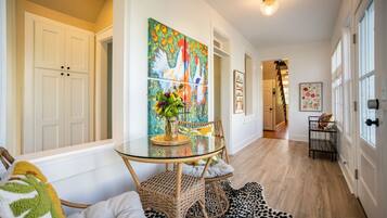 Un couloir avec une table à manger dont le plateau est en verre, des chaises en osier et un tapis à motifs noir et blanc.