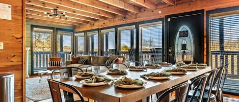 A wooden interior with a dining table set for a meal, large windows, and a cozy seating area.