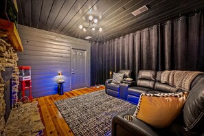 A cozy living room with a leather sofa, a small side table with a lamp, a patterned rug, and a stone wall. - Spacious Cabin with Game Room, Hot Tub & 3 Decks Near Smoky Mountains, Sevierville, TN (Sevierville)