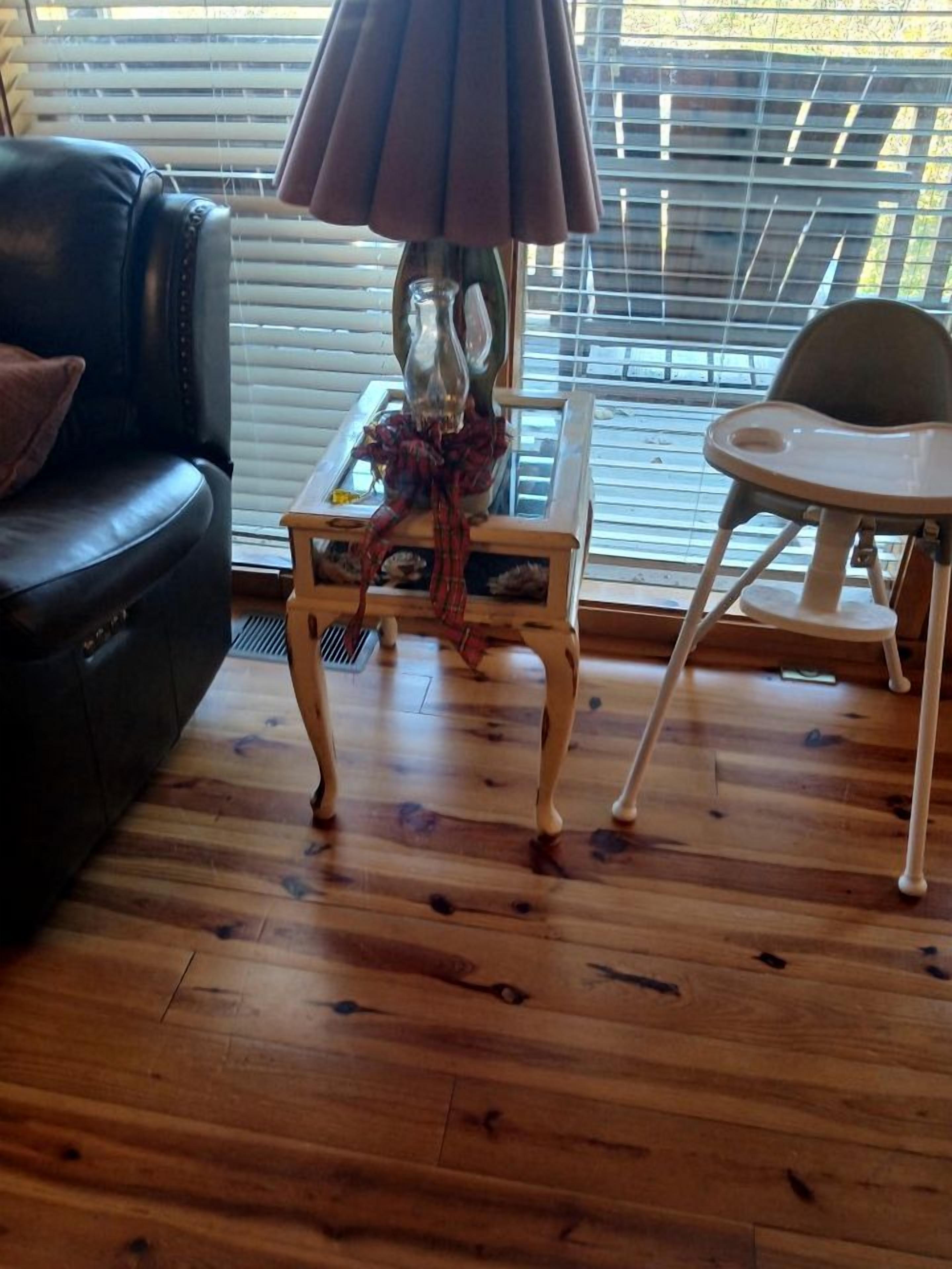 Ein Zimmer mit Holzboden, einer schwarzen Ledersofa, einem kleinen Tisch mit Lampe und einem Stuhl.