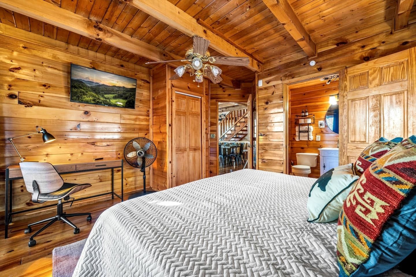A wooden cabin room with a bed, desk, chair, and a ceiling fan.