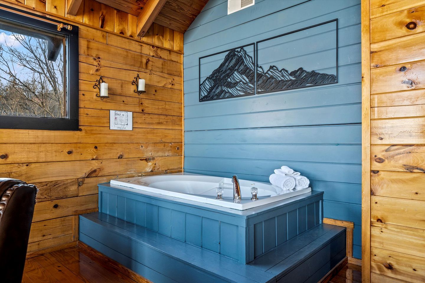 Ein Holzblockhaus-Innenraum mit einer großen Badewanne, Holzwänden und einem Bild mit einer Berglandschaft.