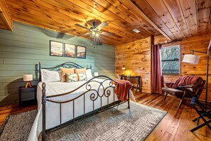 A wooden cabin bedroom with a bed, nightstand, lamp, and a view of the outdoors. - Spacious Cabin with Game Room, Hot Tub & 3 Decks Near Smoky Mountains, Sevierville, TN (Sevierville)