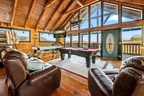 Ein Holzinterieur mit Billardtisch, Ledersesseln und großen Fenstern.