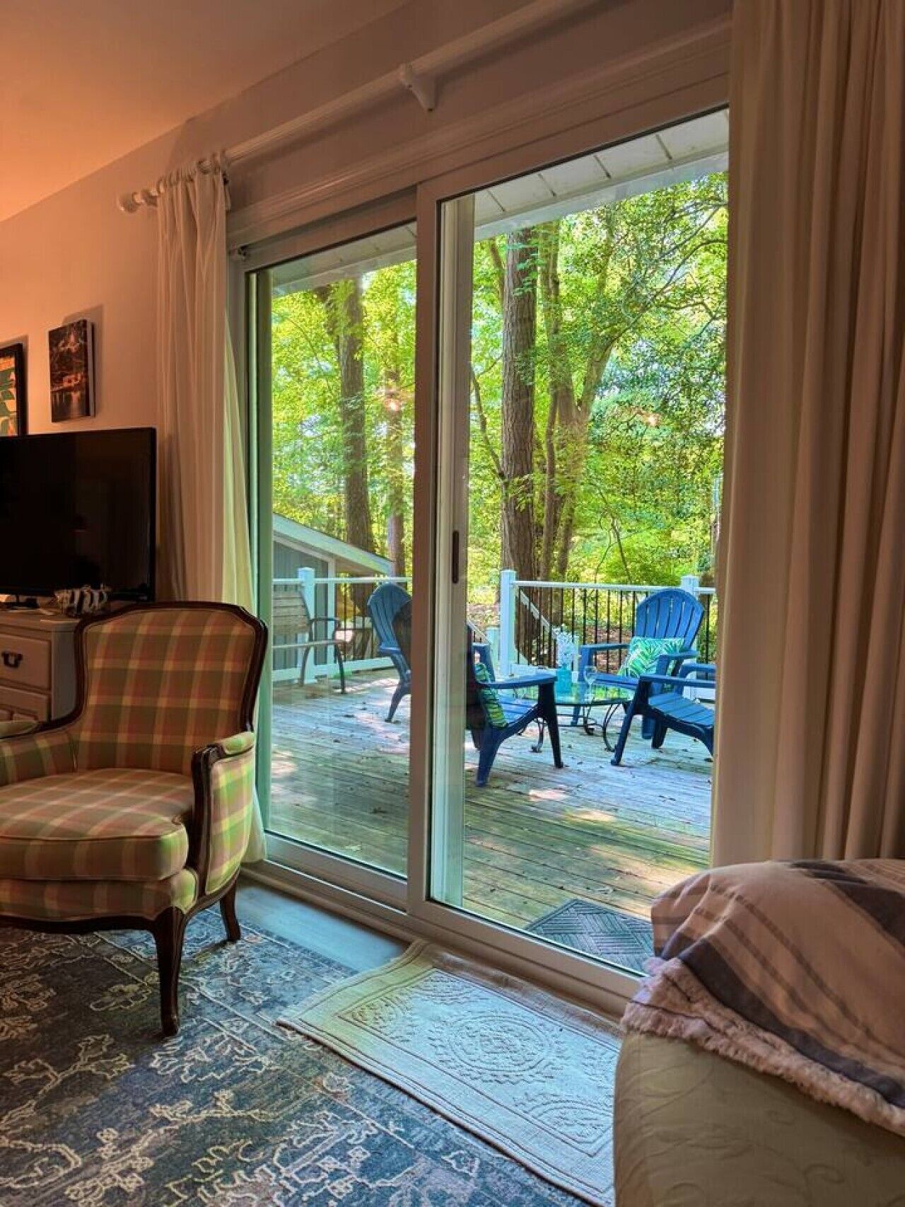 Une pièce dotée d’une grande porte-fenêtre coulissante qui donne sur une terrasse extérieure, avec des chaises et un téléviseur placé dans un coin.