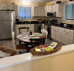 A kitchen with white cabinets, a stainless steel refrigerator, a dining table with placemats, and a basket on the counter. - Quiet family home- Deck, Trails & Water Sports (Ocean Pines)