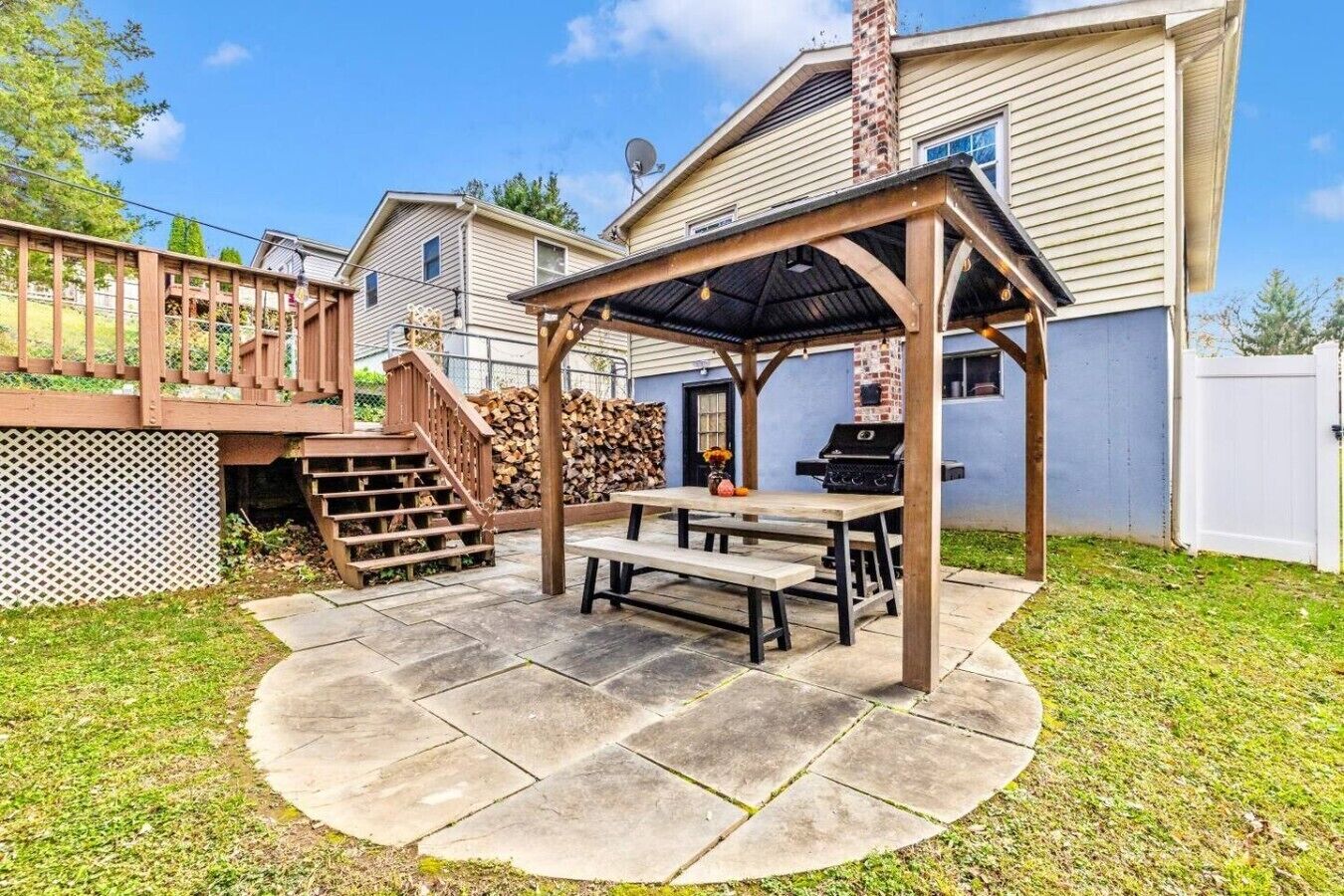 Een achtertuin met een houten pergola, een barbecue en een picknicktafel.