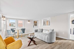 A modern living room with a sofa, chairs, a glass coffee table, and a dining area.