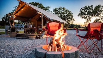 A campsite with a fire pit, a tent, and two red chairs.