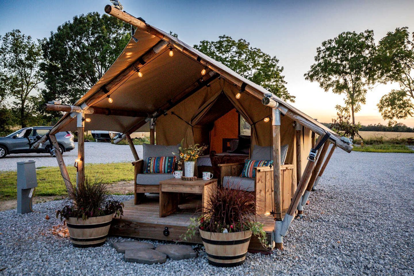 Un hébergement de style rustique, aménagé dans une tente, avec une terrasse en bois, un coin salon et des plantes en pot.