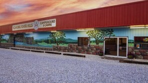 Un terrain de camping avec un bâtiment rouge, une fresque représentant un paysage et un espace de stationnement recouvert de gravier.