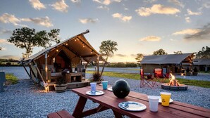 A rustic outdoor dining area with a wooden table, picnic benches, and a fire pit.