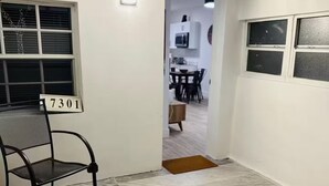 A room with a tiled floor, a chair, a door leading to a dining area, and a number sign '7301' on the wall.
