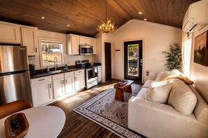 A modern kitchen with stainless steel appliances, a dining area with a white table, and a living room with a beige sofa. - Lakefront Tiny Home Retreat with Private Dock & Sunset Views in Tracy City, Tennessee (Tracy City)