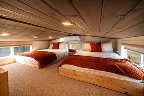 L’intérieur d’une cabane avec deux lits en bois, une fenêtre et un plafond avec des poutres en bois.