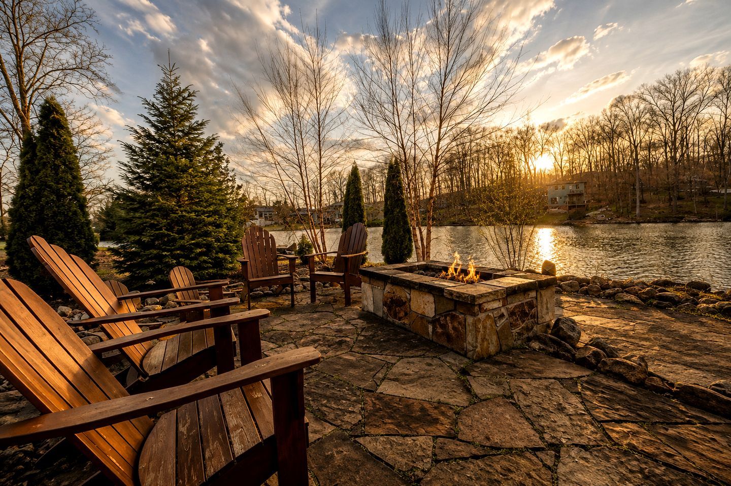 A lakeside seating area with Adirondack chairs and a stone fire pit.