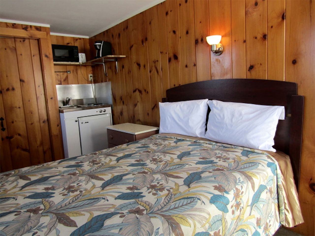 Una habitación con cama, una kitchenette pequeña y paredes de madera.