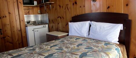 Una habitación con cama, una kitchenette pequeña y paredes de madera.