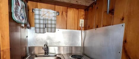 Una cocina compacta con pileta, estufa y microondas, paredes de madera y un respuesto de metal.