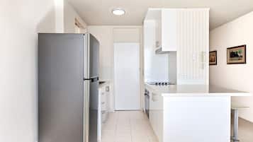 A compact kitchen with a refrigerator, stove, and white cabinetry.
