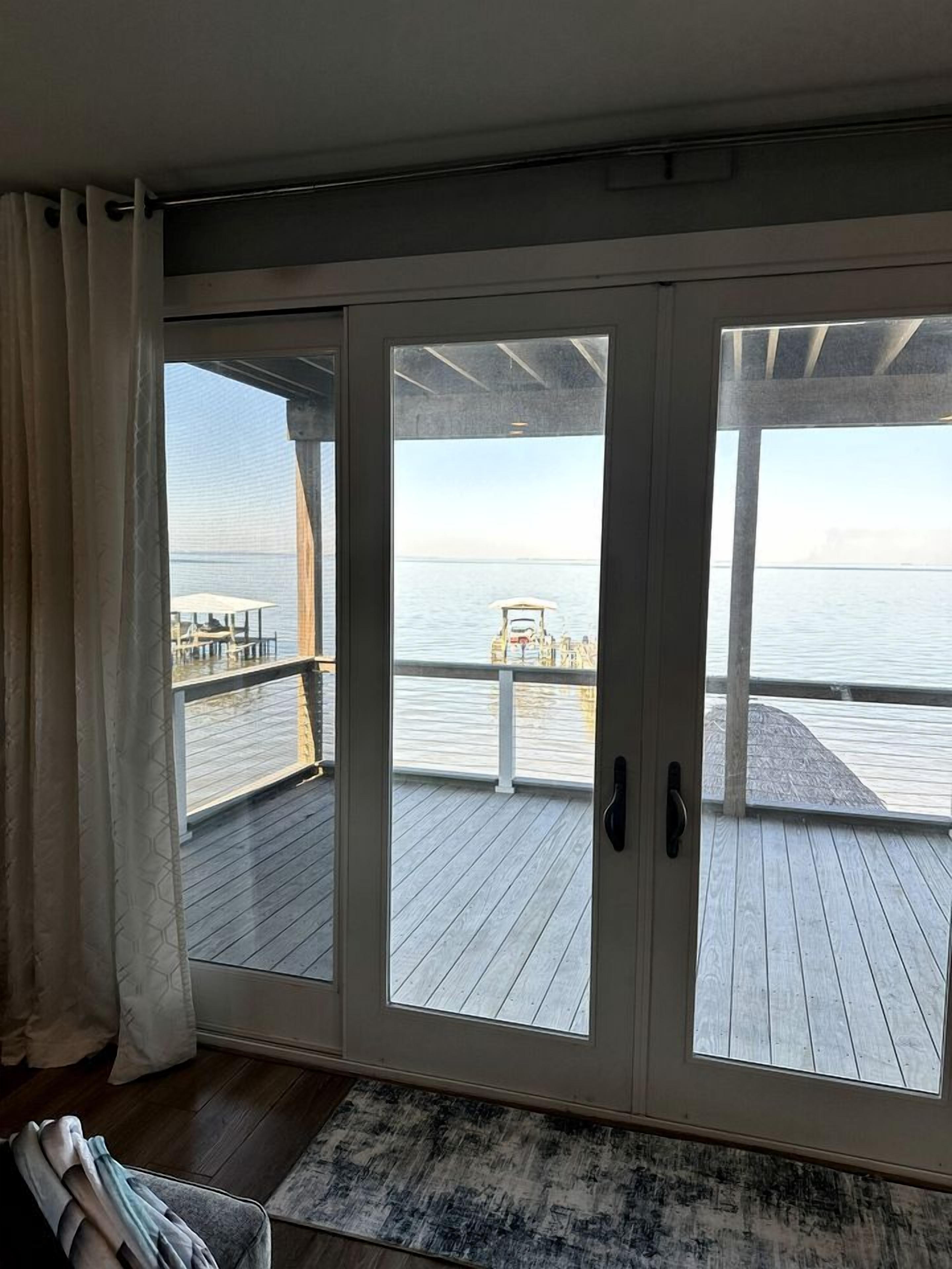 A room with a large sliding glass door leading to a wooden deck overlooking a body of water.