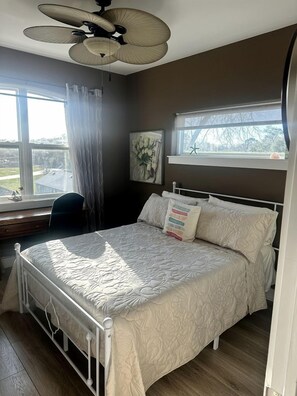A bedroom with a bed, a ceiling fan, a window with curtains, and a painting on the wall. - Luxury Bayfront Escape with Hot Tub & Fireplaces in Bacliff, Texas (Bacliff)