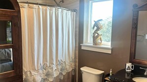 A bathroom with a shower curtain, toilet, sink, vanity, and a window with a view. - Luxury Bayfront Escape with Hot Tub & Fireplaces in Bacliff, Texas (Bacliff)