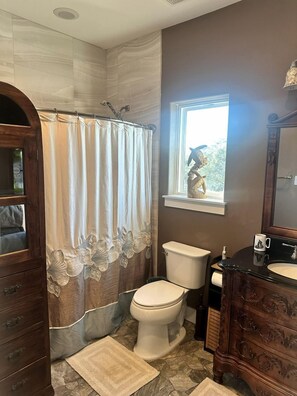 Ein Badezimmer mit Duschvorhang, Toilette, Waschbecken, Waschtisch und einem Fenster mit Blick.