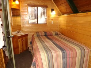 A small, cozy room with a bed, a wooden cabinet, a window, and a door. - Relaxing Cabin Perfect to Disconnect and Recharge in Arizona (Flagstaff)